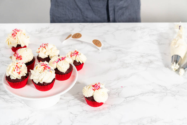 Tubulação de cobertura de ganache de chocolate branco em cima de cupcakes de veludo vermelho e cobertura com polvilhas. - Foto, Imagem