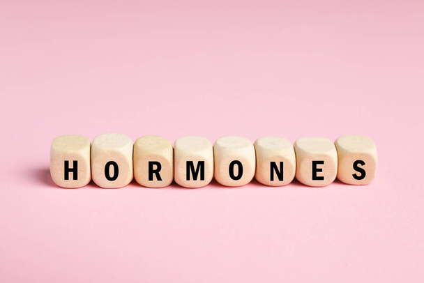 Hormonas Word hechas de cubos de madera con letras sobre fondo rosa - Foto, imagen
