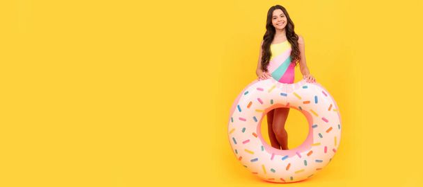 child in swimming suit with doughnut inflatable ring on yellow background, summer. Banner of summer child girl in swimsuit, studio poster header with copy space - Zdjęcie, obraz