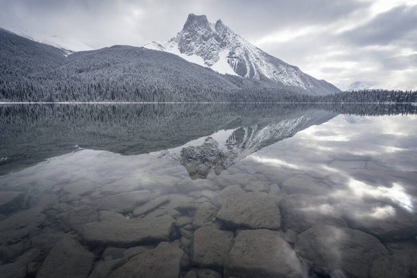 Montaña nevada reflejándose en un lago aún cristalino en un día nublado, Yoho N. Park, Canadá. - Foto, imagen