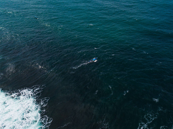 Drone photo of fishing boat in the middle of the ocean looking for fish with cloudy sky on the background - Photo, image