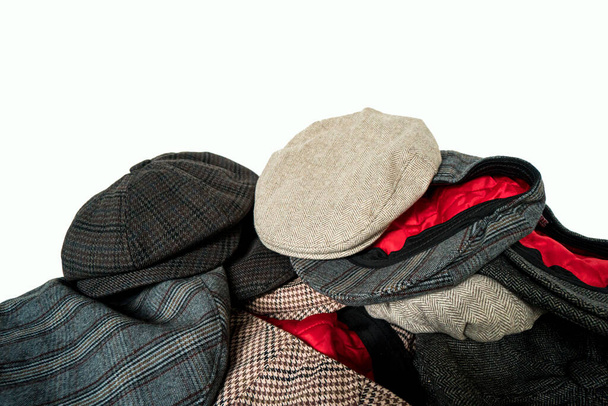 Pile de chapeaux de newsboy classiques et de chapeaux écailleux en tissu tweed de différentes couleurs et motifs sur un fond blanc - Photo, image