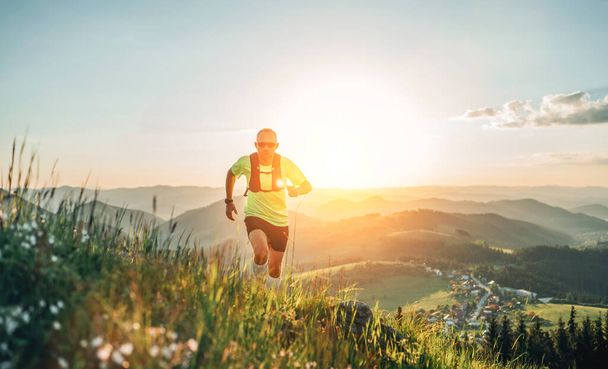 Active mountain trail runner dressed bright t-shirt with backpack in sport sunglasses running endurance marathon race by picturesque hills at sunset time. Sporty active people concept image. - 写真・画像