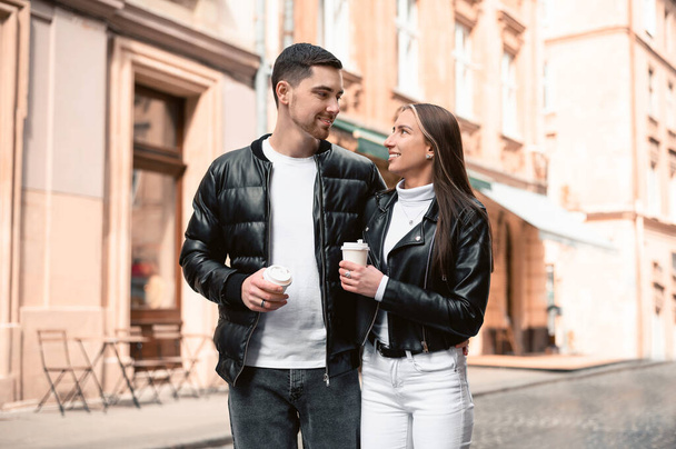 Lovely young couple with cups of coffee walking together on city street. Romantic date - 写真・画像