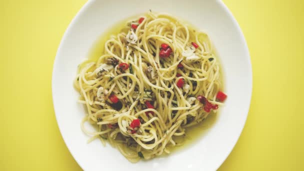 Tradiční italské jídlo. Špagety agilo olio s pikantními chilli papričkami a olivou. Podává se na bílém talíři. Pohled shora, plochý. Žluté pozadí. - Záběry, video