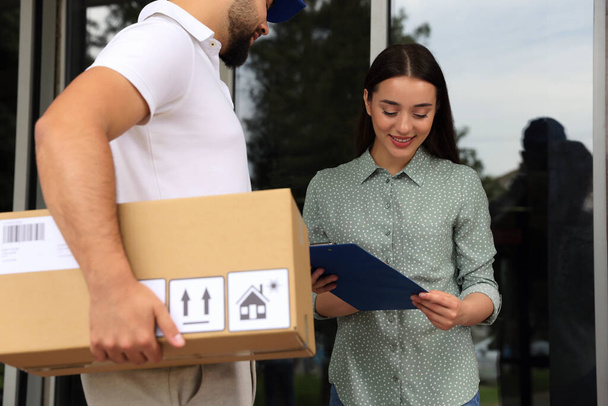Woman signing for delivered parcel near entrance outdoors - Photo, image