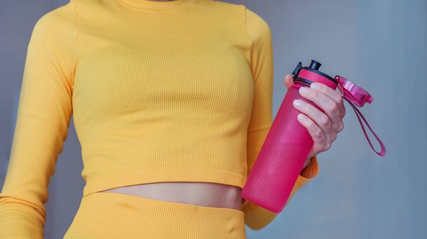 Fit woman with sport outfit holding pink water bottle. Fitness woman drinking water during workout .Hydration during training concept - Foto, afbeelding
