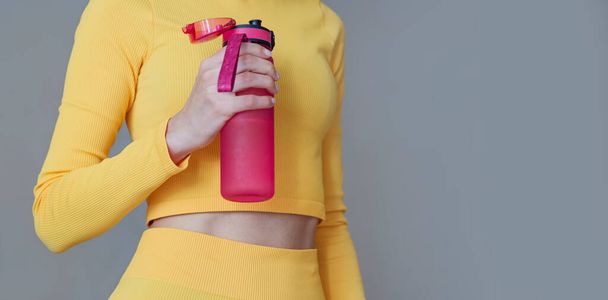 Fit woman with sport outfit holding pink water bottle. Fitness woman drinking water during workout .Hydration during training concept - Фото, изображение
