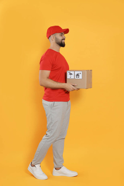 Courier holding cardboard box on yellow background - Фото, зображення