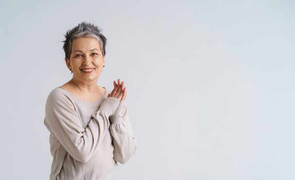 Mature grey hair woman posing with hands folded smiling looking at camera wearing white blouse, copy space on right isolated on white background. Healthcare concept. Aged beauty concept.  - Photo, Image