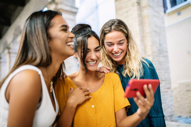 Happy young women having fun together watching funny media content on mobile phone while standing together in city street - Technology and friendship concept - Foto, Imagem