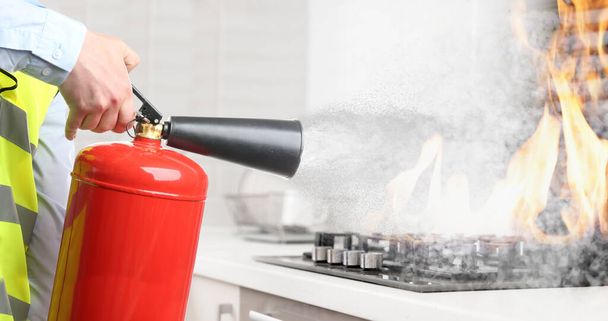 Man putting out burning cooktop with fire extinguisher in kitchen, closeup. Banner design - Fotoğraf, Görsel
