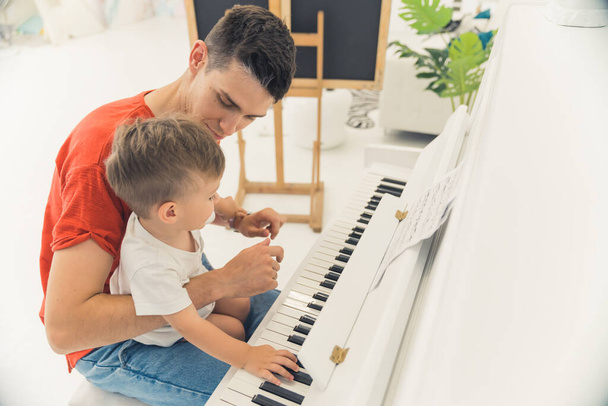 Ο νεαρός πατέρας μαθαίνει στο γιο του να παίζει πιάνο, μέτρια βολή. Υψηλής ποιότητας φωτογραφία - Φωτογραφία, εικόνα