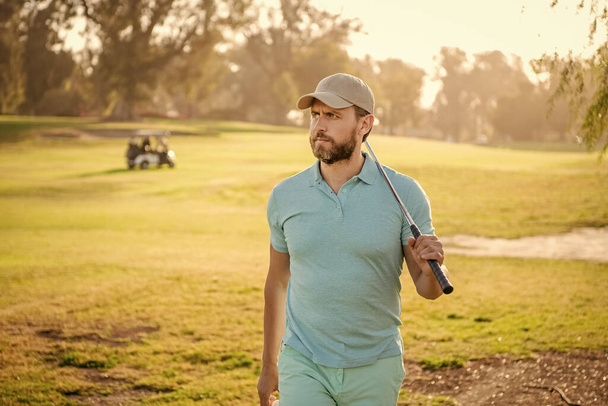 people lifestyle. serious guy after game on green grass. summer activity. professional sport outdoor. male golf player on professional golf course. portrait of golfer in cap with golf club. - Zdjęcie, obraz