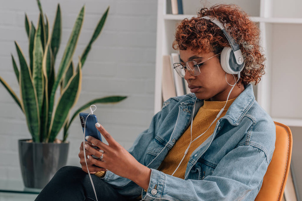девушка дома слушает музыку с наушниками и мобильным телефоном - Фото, изображение
