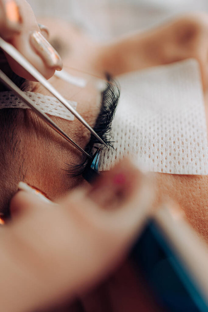 Extreme close up shot of eyelash extension procedure. Cosmetics and body care concept. Shallow depth of field and selective focus. - Zdjęcie, obraz