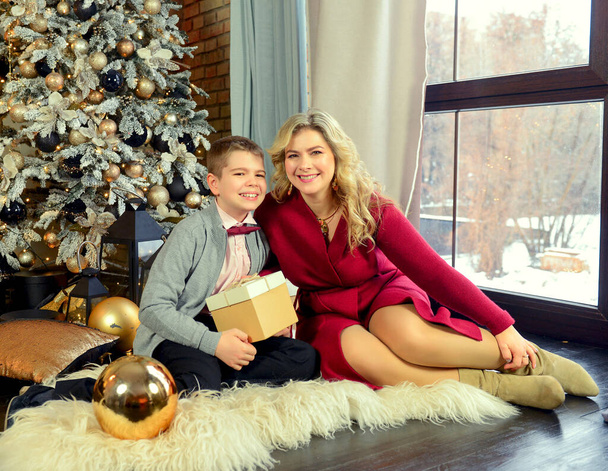 A cute handsome Caucasian boy hugging his mother on a festive day at Christmas. New Year's interior with a Christmas tree. Family traditions. New Year concept. - Foto, imagen