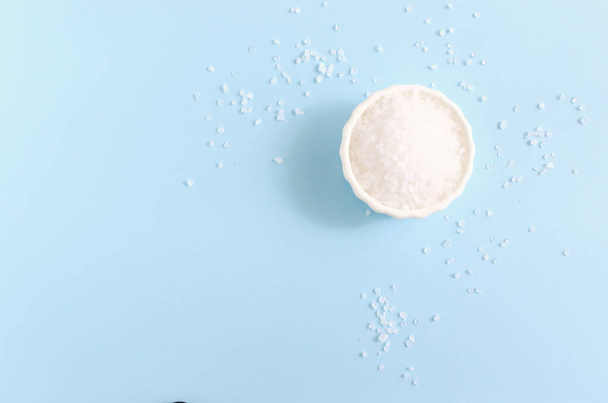 Sea coarse salt in a white ceramic bowl on a blue background. Natural resource. Salt is suitable for cooking and beauty treatments. Horizontal orientation. Copy space. Top view - Foto, Bild