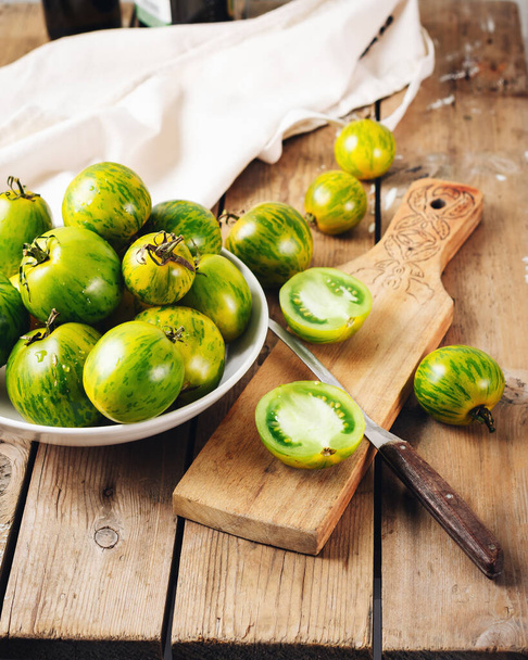 Ωριμάζουν πράσινες ντομάτες σε ένα ξύλινο τραπέζι, σαλάτα μαγείρεμα. - Φωτογραφία, εικόνα
