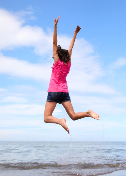 young girl while doing gymnastic exercises and jumping very high near the sea in summer - Foto, imagen