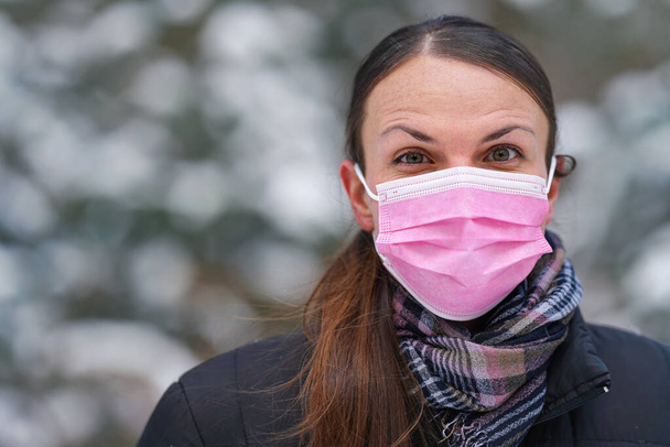 Young woman in winter jacket with pink disposable single use face virus mask - Фото, изображение