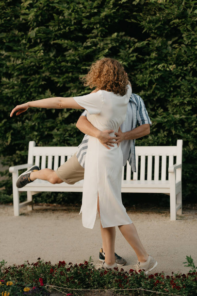 Abends tanzt ein Mann mit einer Frau mit lockigem Haar im Garten. Ein glückliches Paar mit grünen Blättern im Hintergrund. - Foto, Bild