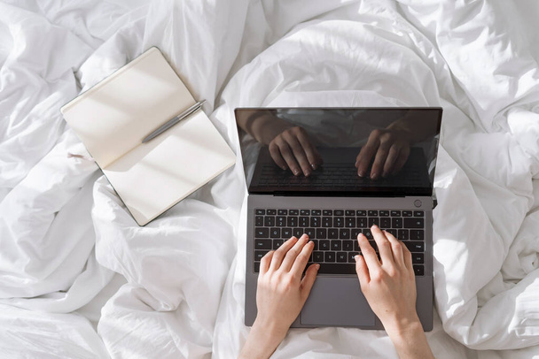 High above view of person's hand typing on laptop keybord when lying in bed, work time, freelancer's lifestyle, busy people, modern technology - Foto, Imagem
