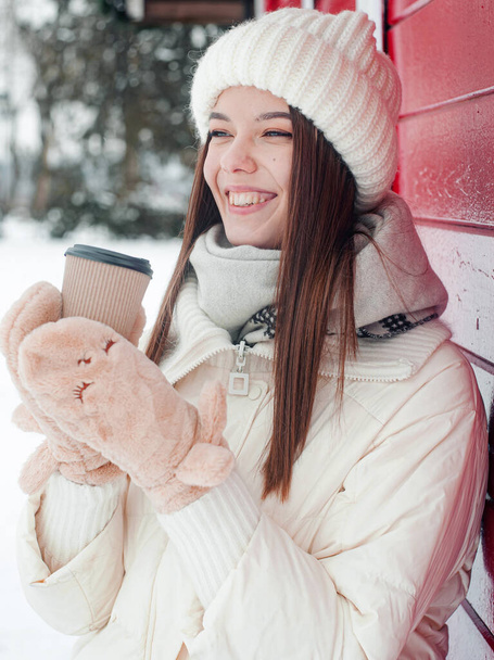  Портрет жінки, яка п'є чай на відкритому повітрі. Молода жінка з чашкою гарячого напою розважається в парку в сніжну погоду
. - Фото, зображення