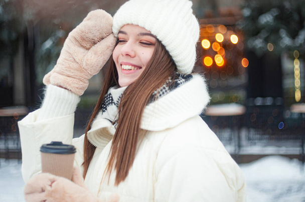  Portrait of woman drinking tea outdoors. Young woman with a cup of hot drink has fun in park in snowy weather. - Photo, Image