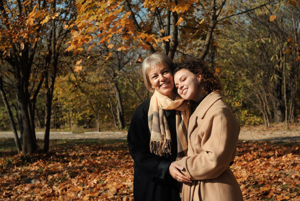 Middle aged woman and young curly hair woman walking in autumn park.Mother and daughter relationship - Photo, Image