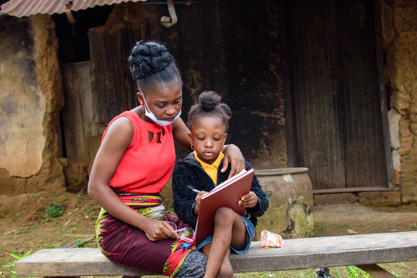 Madre africana o insegnante fuori da una casa di fango con maschera nasale, aiuta una bambina con i suoi studi per l'eccellenza nella sua scuola, carriera e istruzione. - Foto, immagini