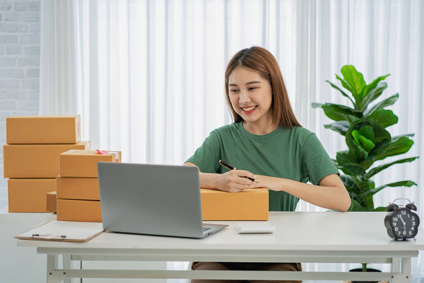 Independent SME Small Business Entrepreneur Portrait of an Asian woman working at home with a laptop taking orders and Online Marketing Packaging Shipping Boxes eCommerce business idea - Фото, зображення