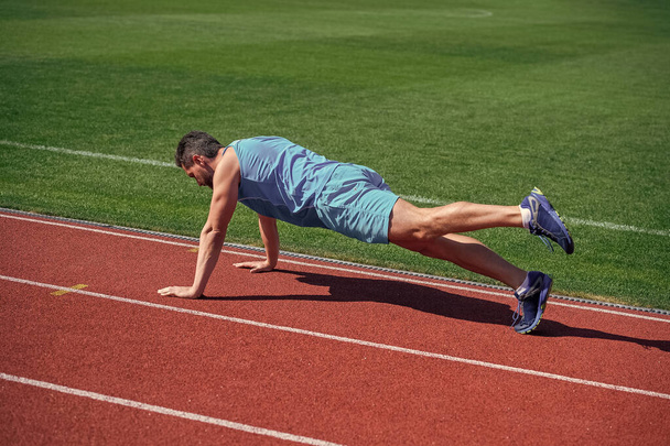 athletic muscular man doing plank outdoor on stadium, core. - Foto, afbeelding