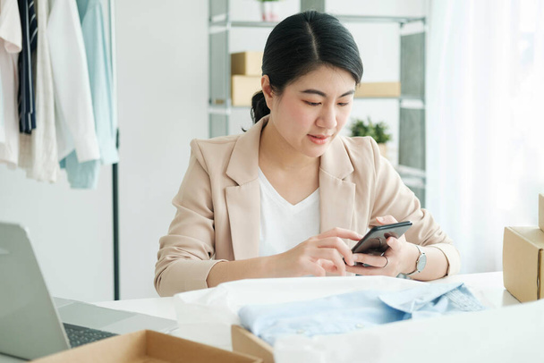 Junge asiatische Unternehmerin Startup-Unternehmerin KMU Besitzer nimmt ein gelbes Hemd, bevor sie es in eine innere Schachtel mit einem Kunden verpackt. Online-Geschäftsideen und Freiberufler. - Foto, Bild