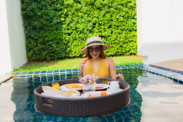 Portret mooie jonge aziatische vrouw gelukkig glimlach ontspannen met ontbijt zweven rond zwembad in hotel resort - Foto, afbeelding