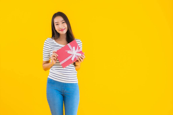 Muotokuva kaunis nuori aasialainen nainen näyttää punainen lahja laatikko keltainen eristetty tausta - Valokuva, kuva