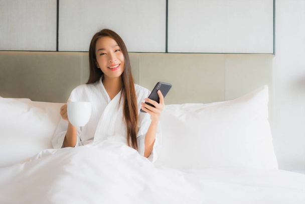 Portré gyönyörű fiatal ázsiai nő használ okos mobiltelefon a hálószobában belső - Fotó, kép