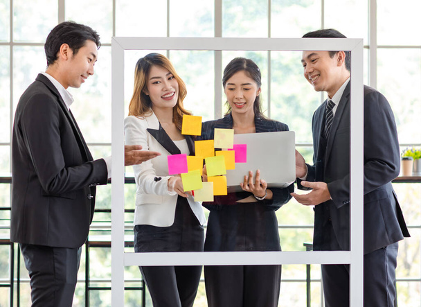 Asian young millennial professional successful male businessman and female businesswoman employee colleague in formal suit stand smiling discussing brainstorming with colorful post it on glass board. - Foto, Imagem