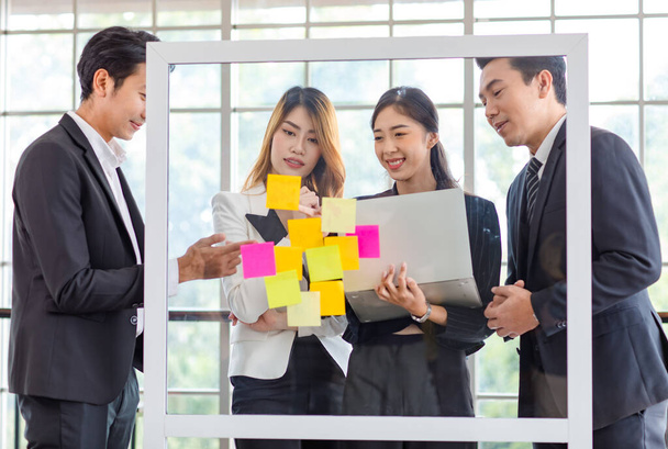 Asian young millennial professional successful male businessman and female businesswoman employee colleague in formal suit stand smiling discussing brainstorming with colorful post it on glass board. - Fotó, kép