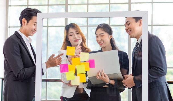 Asian young millennial professional successful male businessman and female businesswoman employee colleague in formal suit stand smiling discussing brainstorming with colorful post it on glass board. - Foto, immagini