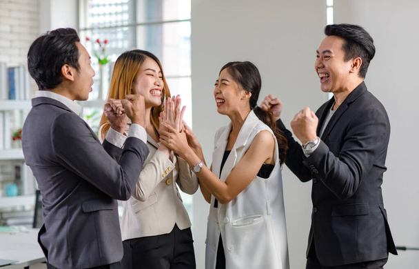 Grupo de asiático feliz alegre millennial profesional exitoso hombres de negocios y mujeres de negocios en traje formal de pie cogidas de la mano levantaron los puños celebrando el logro del trabajo juntos. - Foto, Imagen