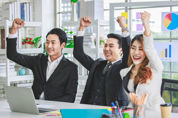 Group of cheerful Asian millennial professional successful male businessman and female businesswoman in formal suit sitting smiling holding fists up together celebrating customer agreement deal done. - Photo, image