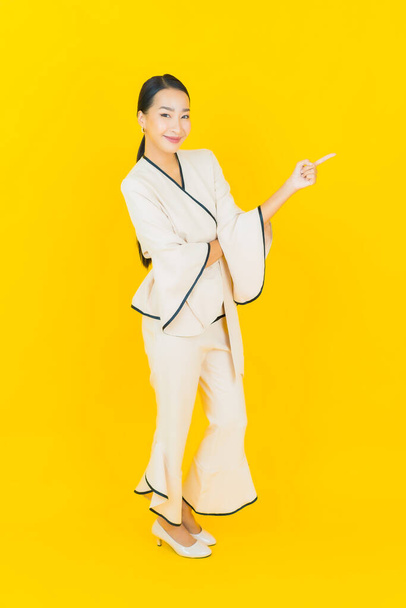 Portré gyönyörű fiatal üzleti ázsiai nő mosollyal és akció sárga háttér - Fotó, kép