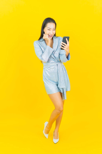 Portrait beautiful young asian woman smile with smart mobile phone on yellow color background - Foto, imagen