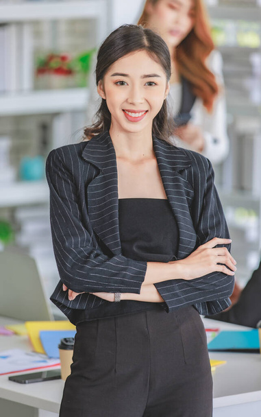 Portrait shot Asian young happy cheerful confident millennial professional successful female businesswoman in formal suit sitting crossed arms smiling while colleagues working in blurred background. - Foto, immagini
