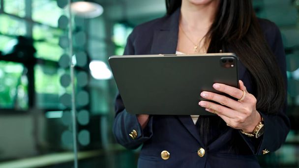 Cropped image, Attractive businesswoman in formal suit standing at the office entrance door and using digital tablet. - Fotoğraf, Görsel