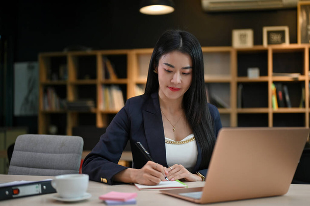 Succesvolle en aantrekkelijke jong-volwassen Aziatische zakenvrouw of vrouwelijke executive manager is gericht op haar taak aan het bureau. - Foto, afbeelding