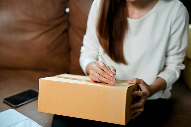 Женщина пишет адрес на картонной коробке. Женщина-владелец интернет-магазина готовит пакет доставки. обрезанное изображение - Фото, изображение