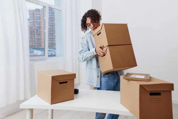 guy with curly hair unpacking things from boxes in the room Lifestyle. High quality photo - Photo, Image