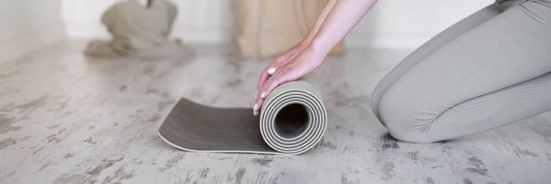 Close-up of a womans hands rolling up a yoga mat. Banner for yoga studio. The concept of a healthy lifestyle. - Zdjęcie, obraz